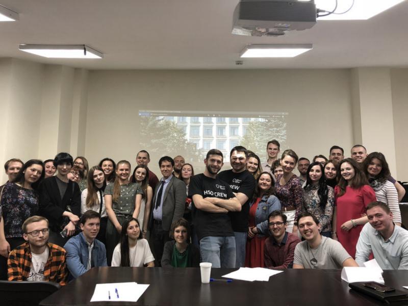 A large group of Higher School of Oncology residents, candidates and organisers in a conference room in 2018, two of them in black HSO Crew T-shirts.